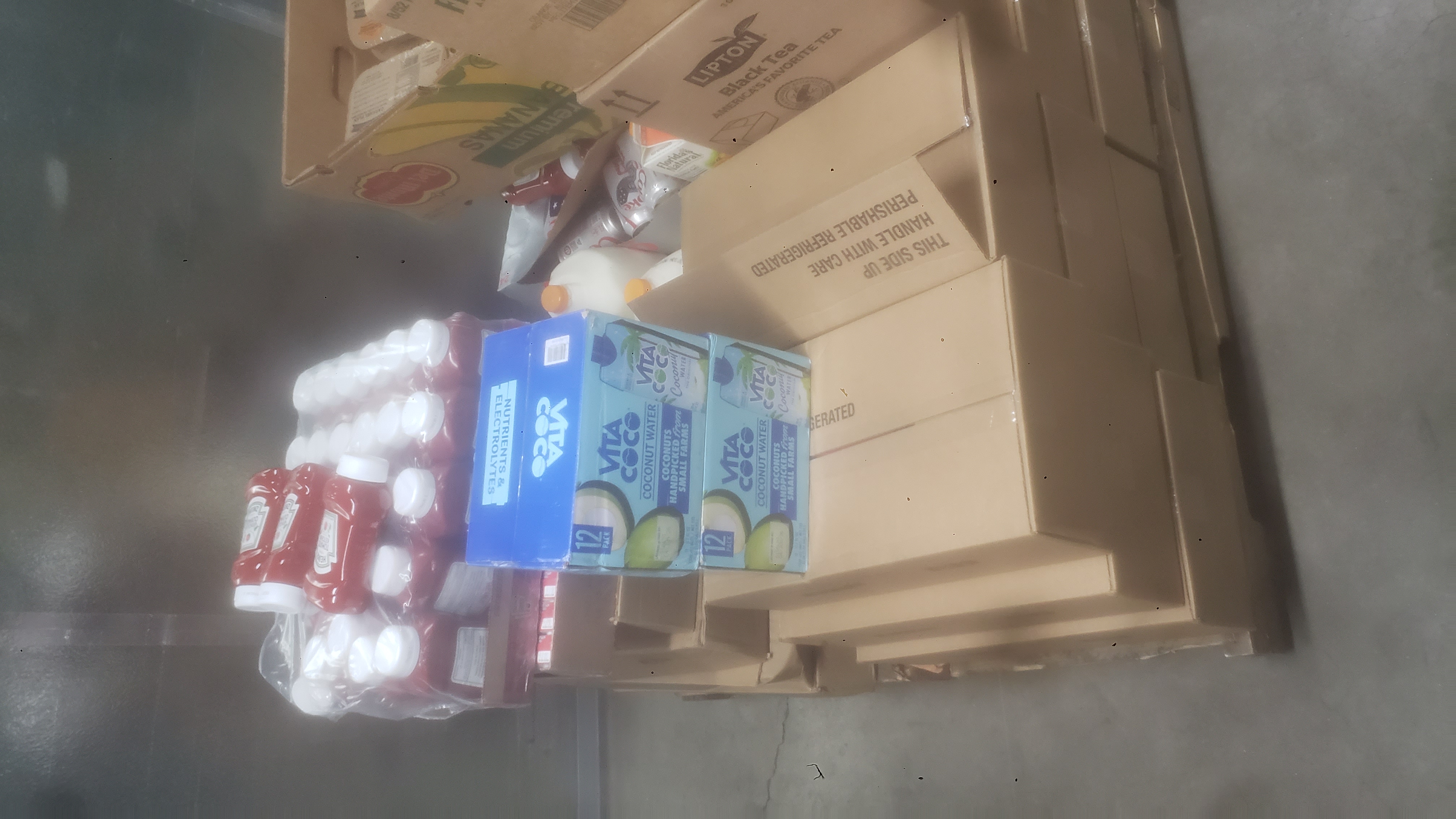 Case of ketchup, case of juice boxes, and boxes of coconut water on top of cardboard boxes.